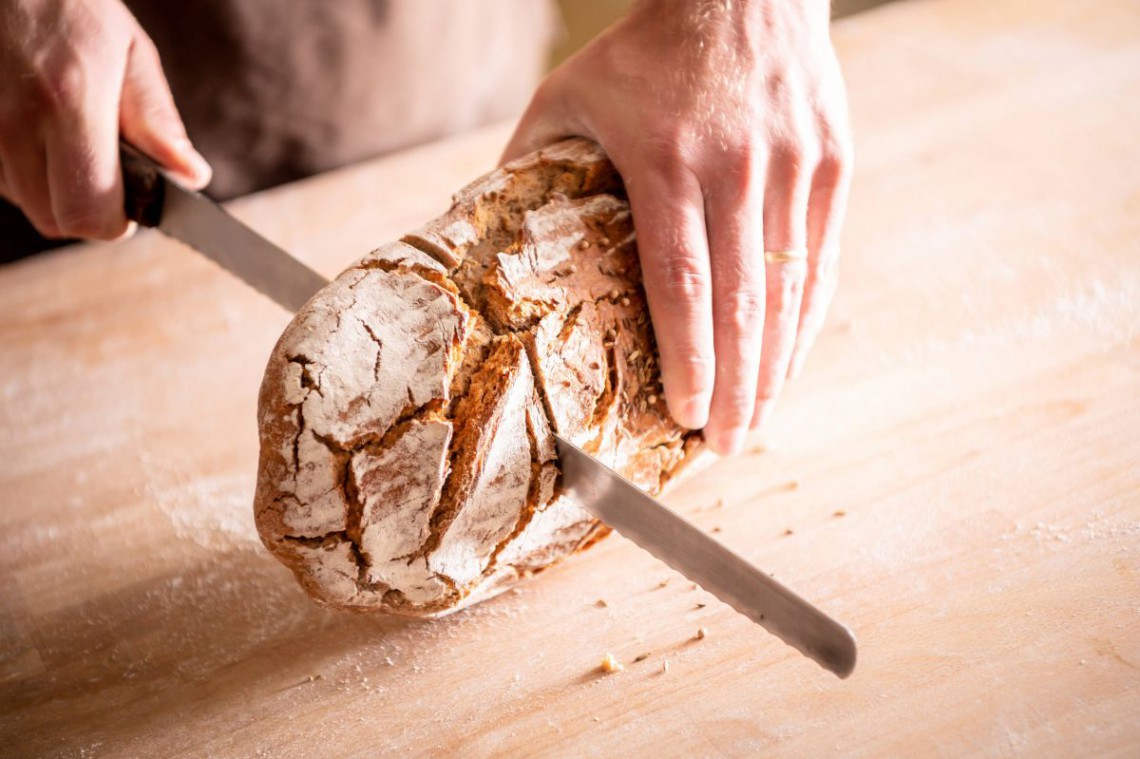 Zwei Händen schneiden einen Laib Brot in der Mitte