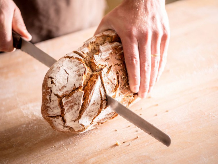 Zwei Händen schneiden einen Laib Brot in der Mitte